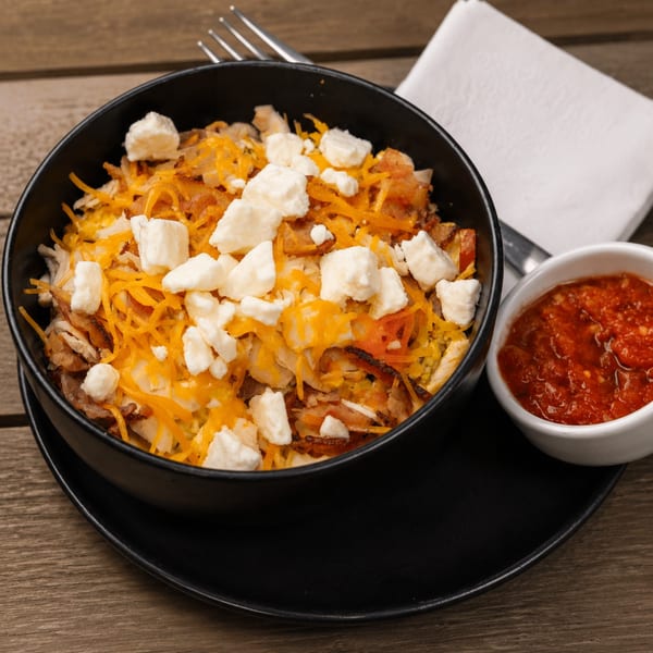 A black bowl of breakfast hash with shredded cheese and feta, served with a side of salsa.