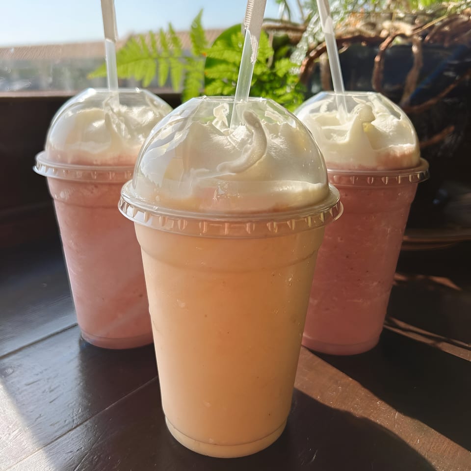 Three vibrant smoothies with whipped cream and straws, two pink and one orange, on a dark wooden surface.