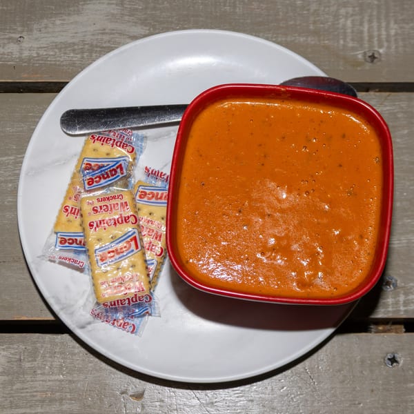 A red bowl of tomato soup with three packets of Captain's Wafers crackers on a white plate.