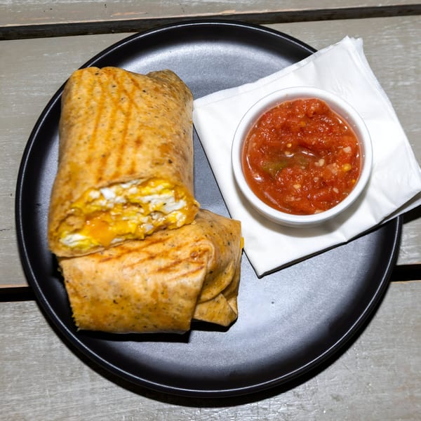 Breakfast burrito with egg and cheese, cut in half, served with a side of salsa.
