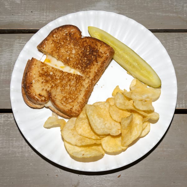 Grilled cheese sandwich with melted cheese, potato chips, and a pickle spear on a white plate.