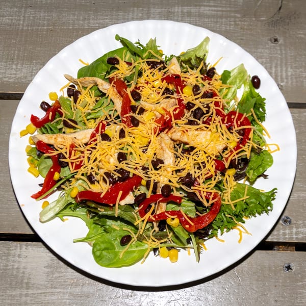 A vibrant chicken salad with mixed greens, red peppers, corn, black beans, and shredded cheese.