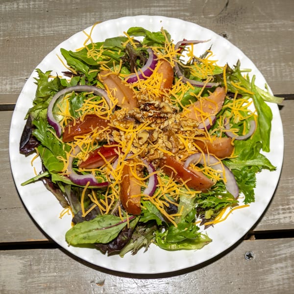 A fresh salad with mixed greens, red onion, dates, walnuts, and shredded cheese on a white plate.