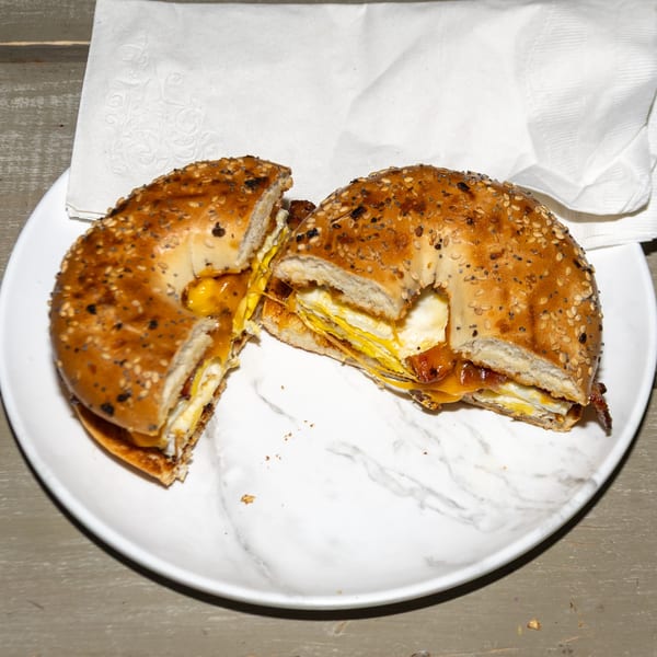 Everything bagel breakfast sandwich with egg, cheese, and bacon, cut in half on a white plate.